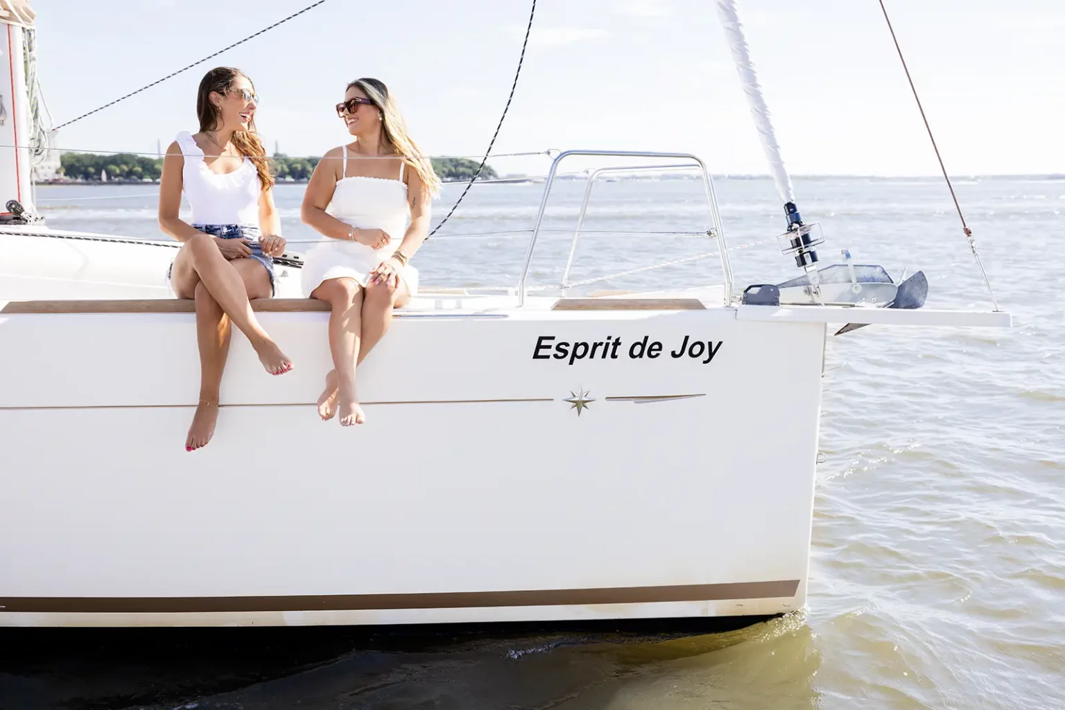 Two friends sitting on the side of Esprit de Joy during a private sailing charter in Charleston Harbor
