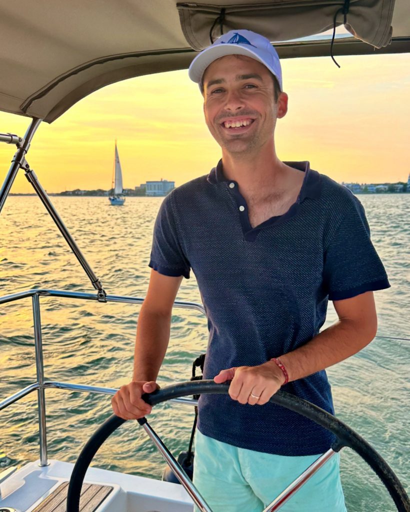 Captain Will Monts smiling at the helm of Esprit de Joy at sunset in Charleston Harbor