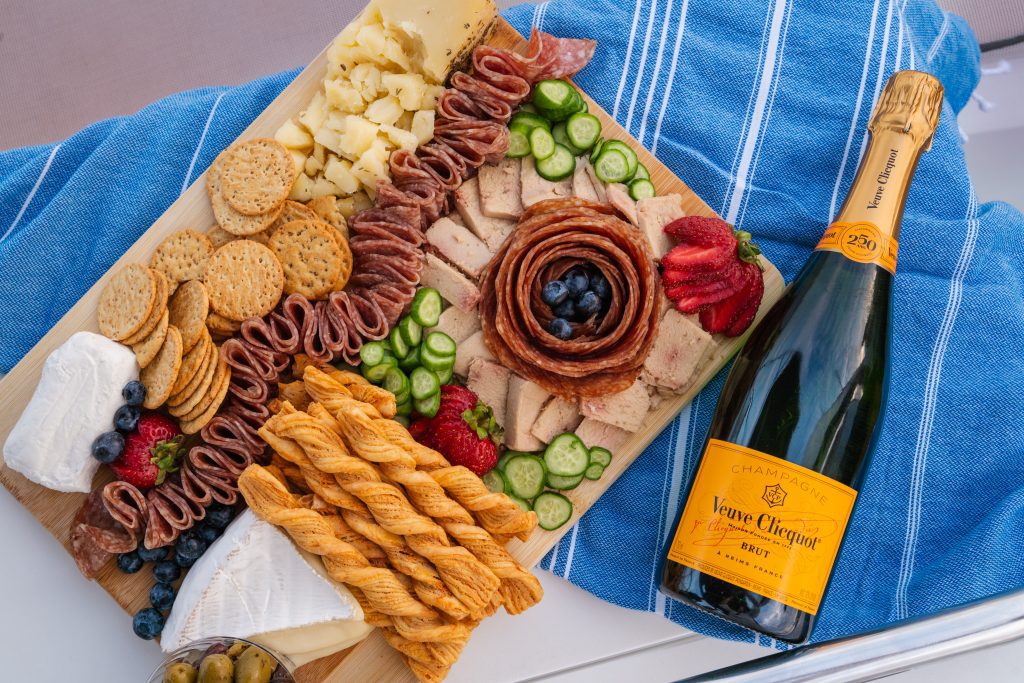 Charcuterie board and a bottle of champagne on a blue towel aboard a private sailboat charter in Charleston